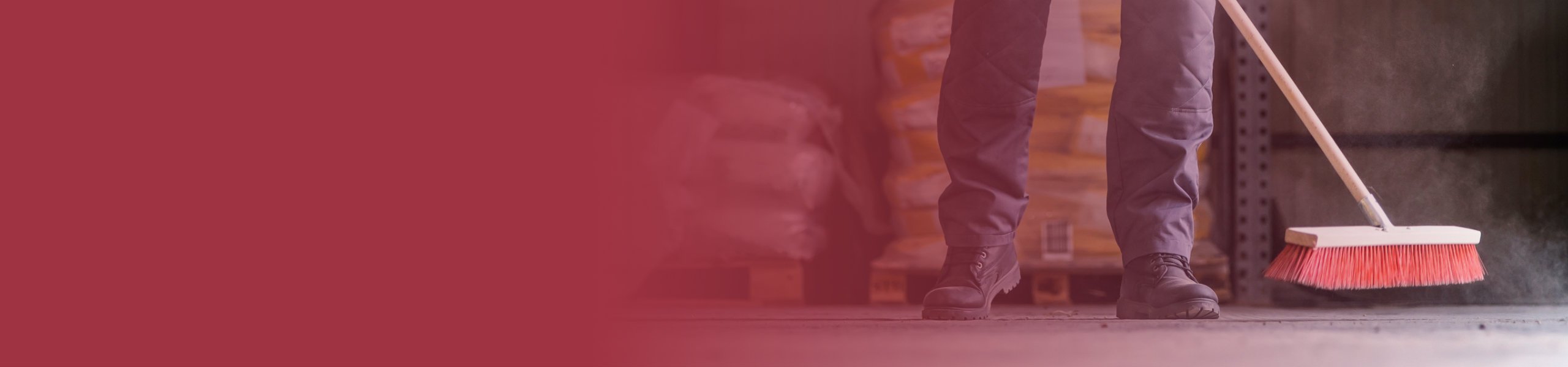 Anschnitt von Beinen einer Person beim Fegen einer Werkstatt.
